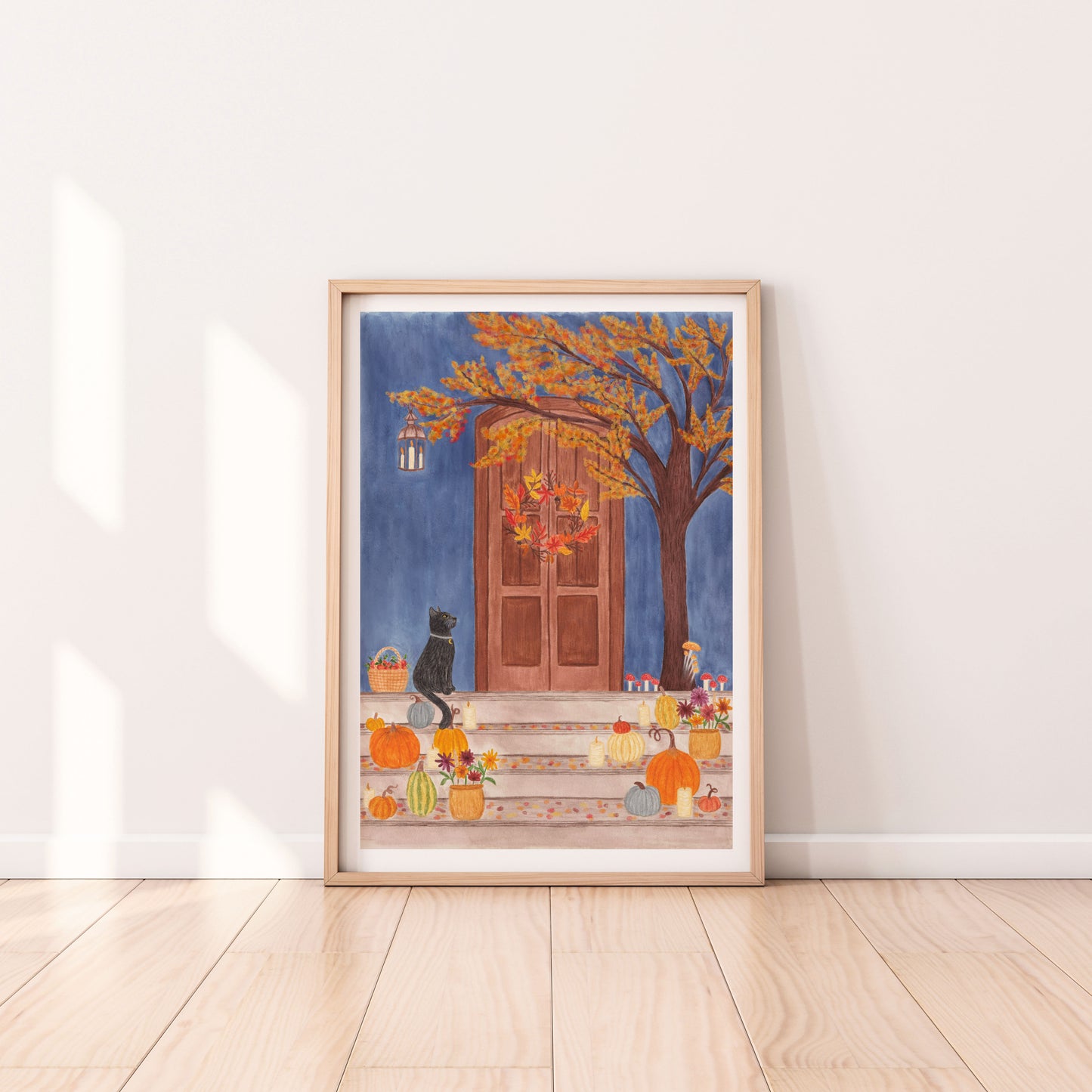 An Autumnal door print, which was originally hand painted with watercolours. Dark blue background with brown door with autumn wreath. Autumnal tree with red and orange mushrooms leaning in front of door. A black cat with a moon collar and a basket of apples on the left. Steps with multicoloured pumpkins, candles and potted plants with autumn flowers.