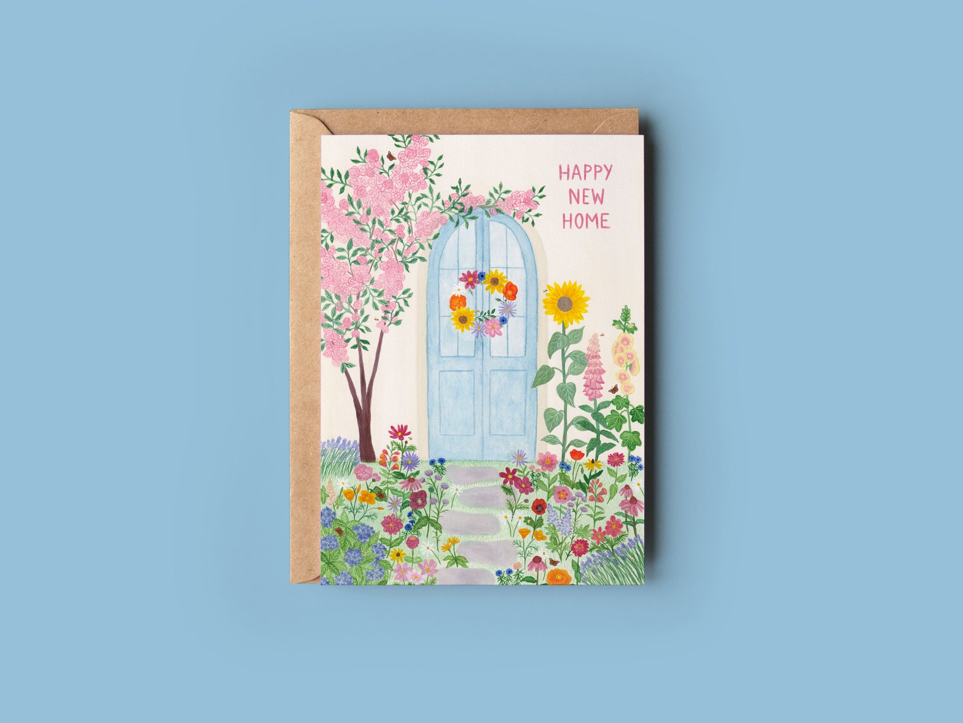 A happy new home greeting card which was originally hand painted with watercolours. Blue door with a summer wreath. Grey stepping stones towards the door with summer flowers surrounding in the grass. Including sunflowers, dahlias, Hollyhock, poppies, foxglove, lupins, echinacea, lavender, hydrangea, daises, cosmos, zinnias, cornflowers as well as peacock butterflies and bees. A pink rose bush tree leaning on door. Text “Happy new home” on the right side.