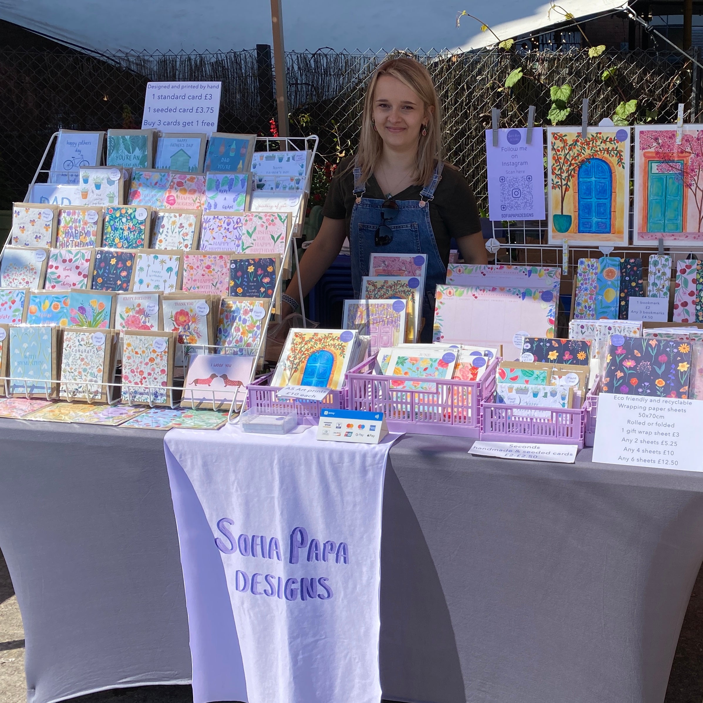 Sofia standing behind a stall displaying various cards, art prints and stationery at Tobacco factory market in Bristol. Sofia Papa Designs