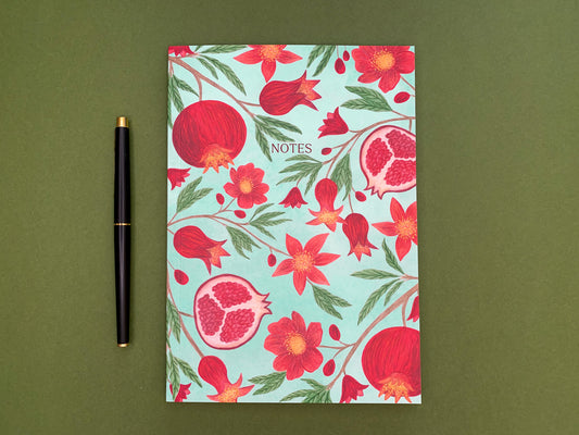 Pomegranate A5 notebook. Pale green watercolour background. Vibrant red pomegranates and flowers pattern with green leaves. The text notes added on the front cover.