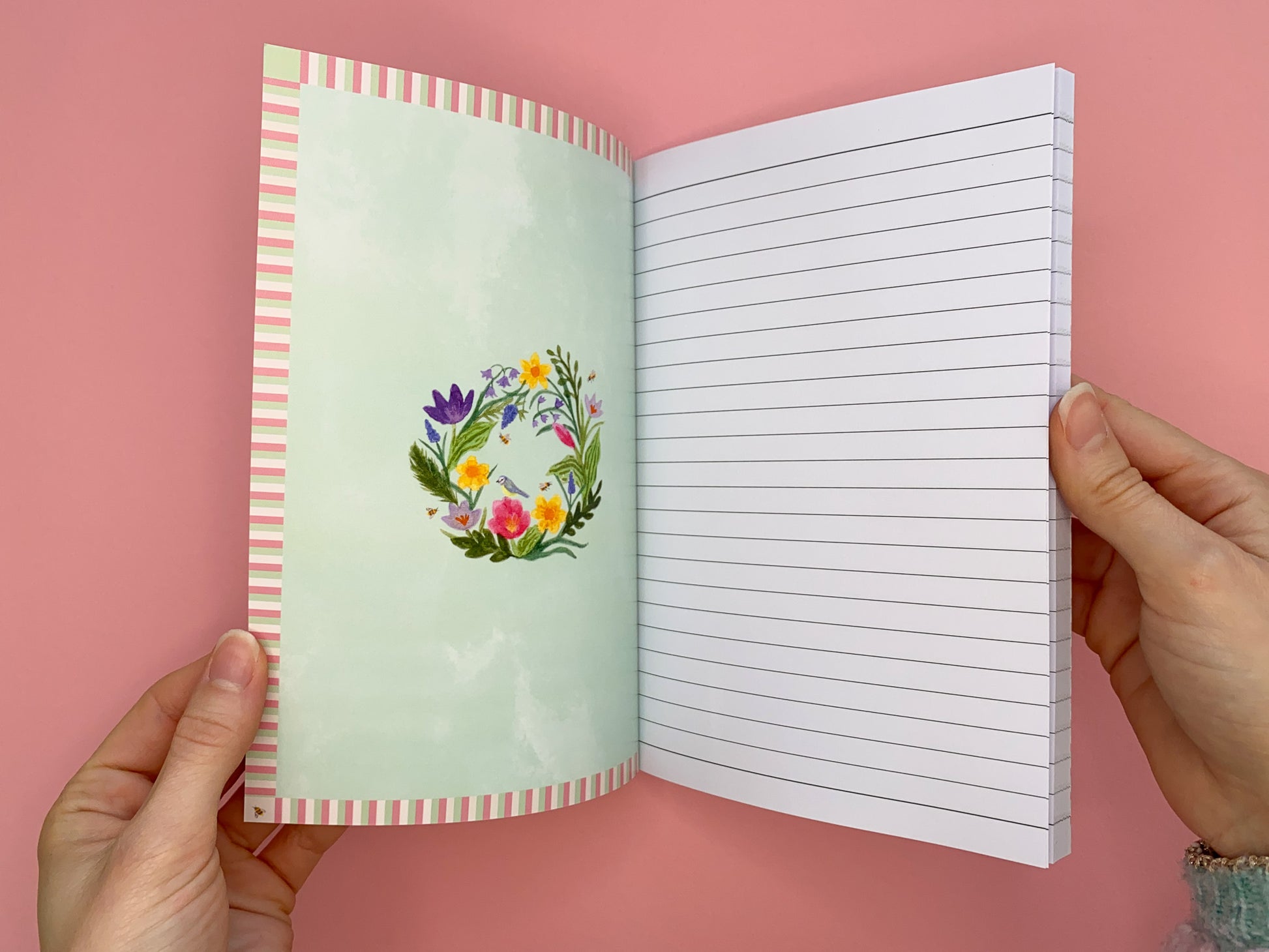Inside front cover design. Stripy border with the spring wreath in the middle. Wreath includes daffodils, tulips, bluebells, crocuses, green foliage, bees and a blue tit bird. Same design on the inside back cover.