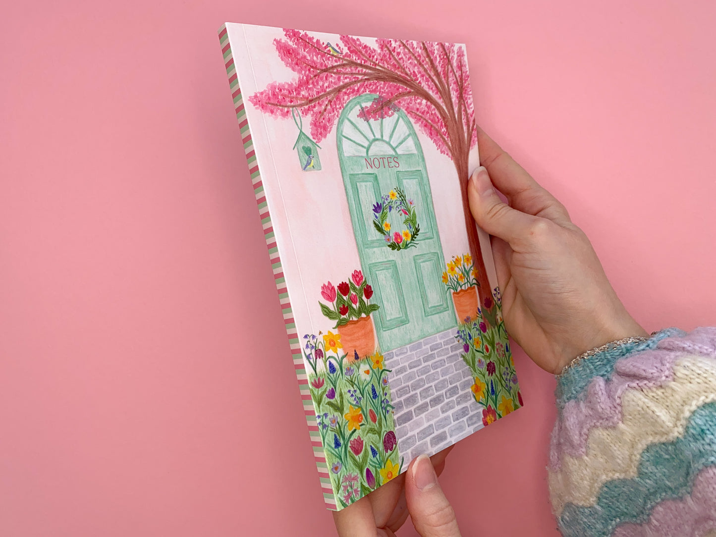 Spine of Spring door notebook. The spine has a stripy pattern with pastel pale pink, green and darker pink.